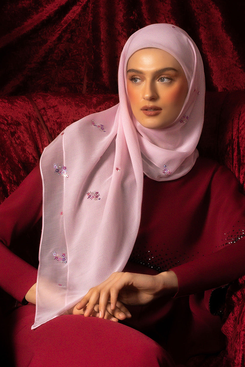 A woman wearing bawal in law with floral patterns and a baby seam, sitting against a red backdrop.